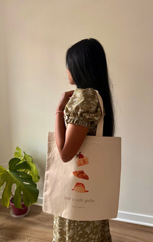 Person holding a tote bag with illustrations and text, standing indoors.