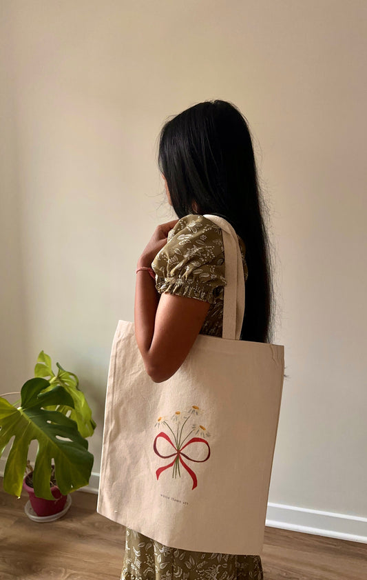 Person holding a beige tote bag with a red bow design indoors.