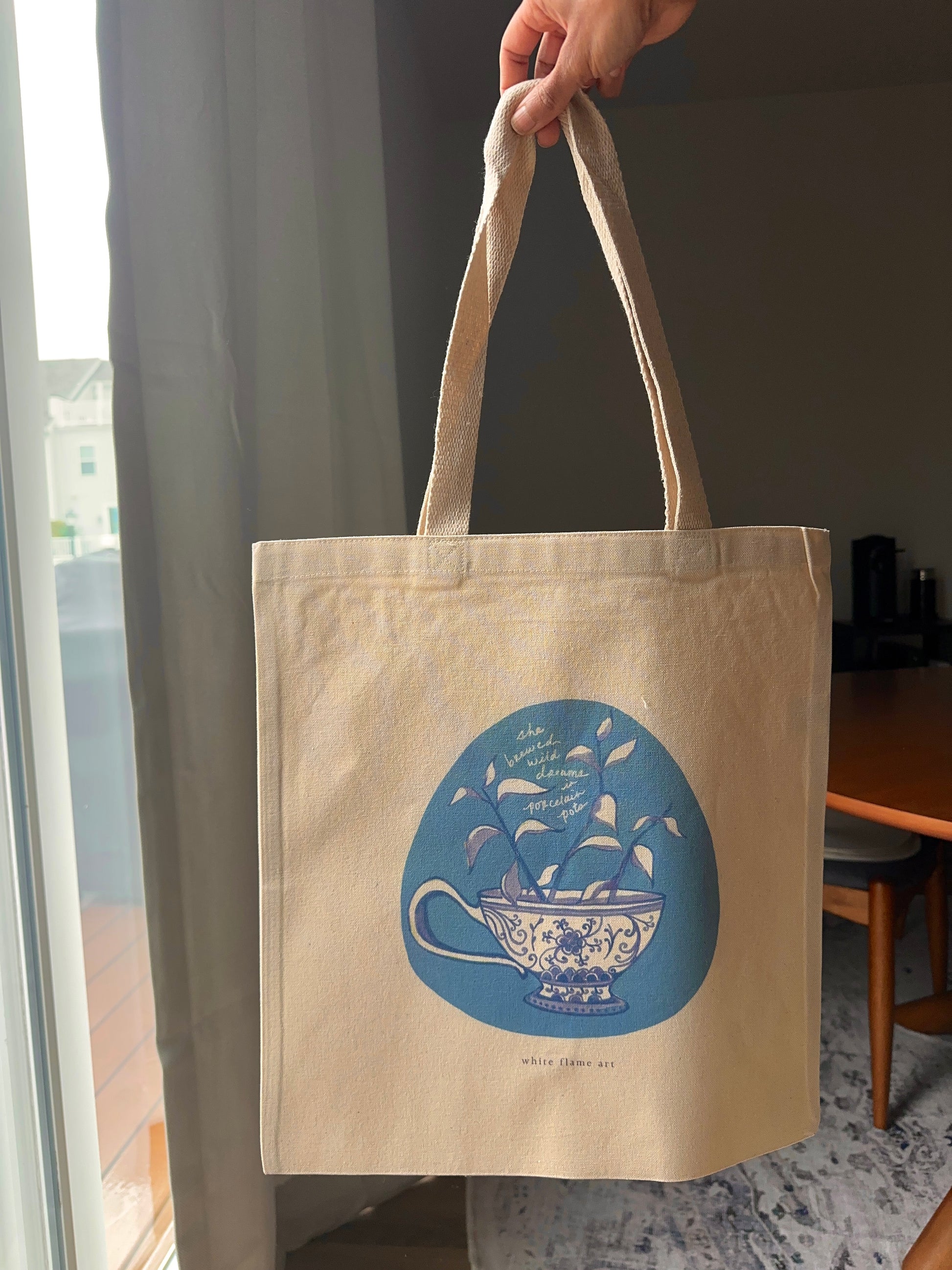 Beige tote bag with blue design held by a hand indoors.